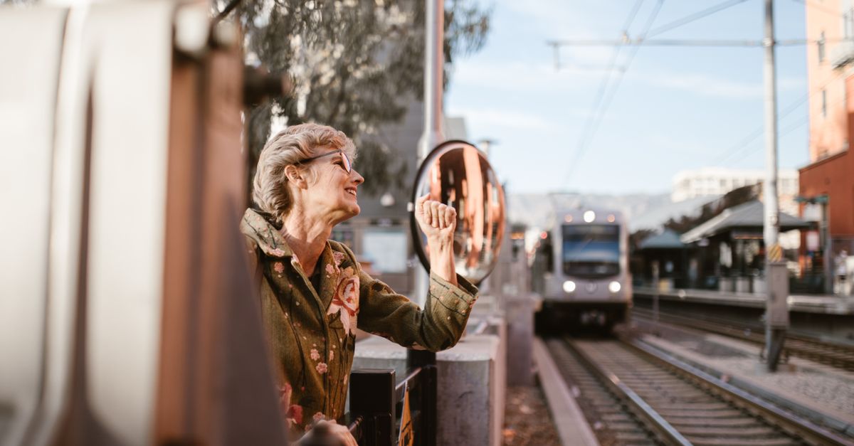 Senior woman making a fist at a train station with an urban train arriving, capturing a moment of lively expression.