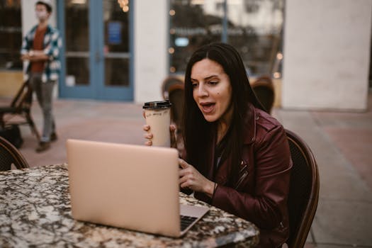 Woman in a leather jacket holding a cup and chatting online at a cafe table.