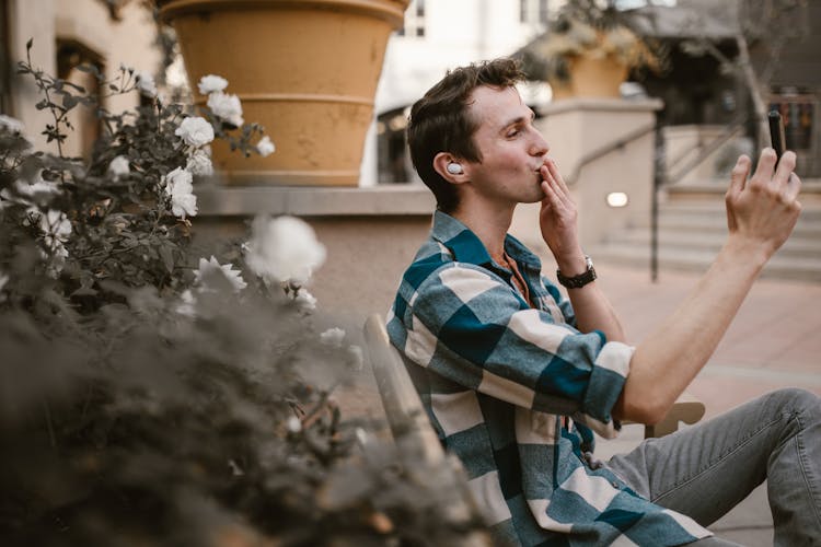 A Man In Plaid Long Sleeves Talking On The Phone With His Hand On His Mouth