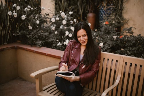 A Woman Sitting on a Wooden Bench while Holding a Notebook