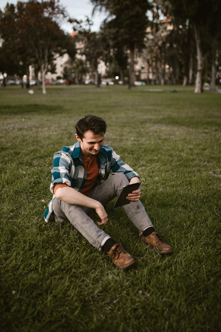 A Man Sitting On The Field While Holding His Tablet