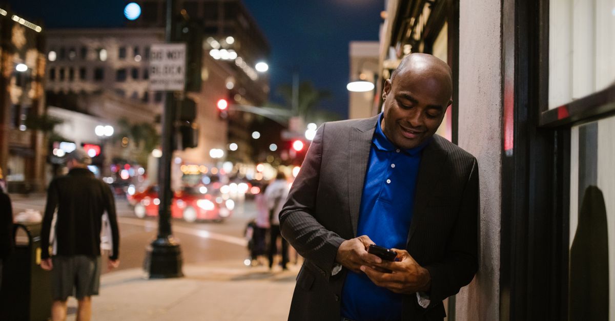 Man leaning against a wall at night, checking his phone