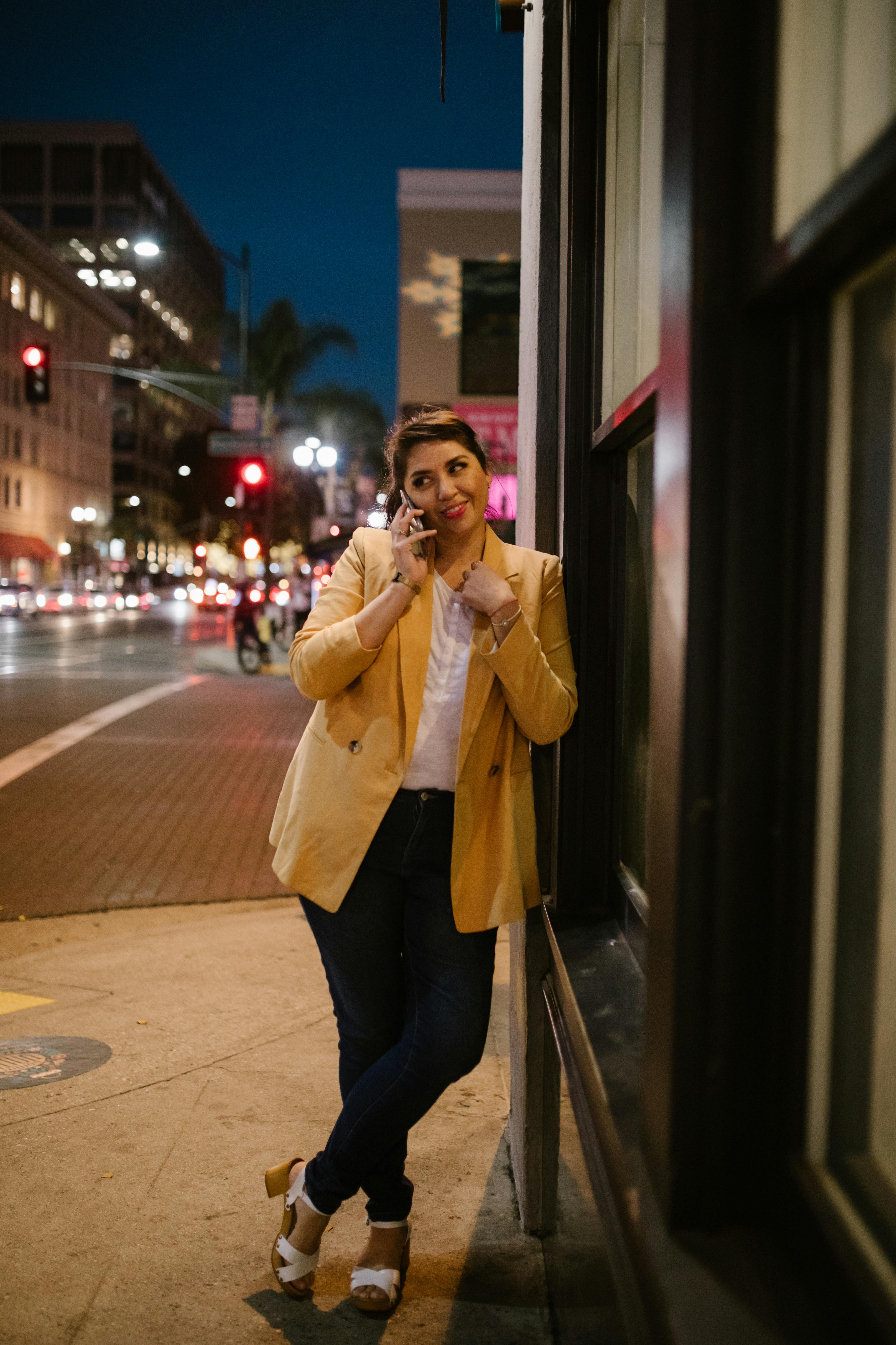 woman in beige coat and black pants standing beside building during night time