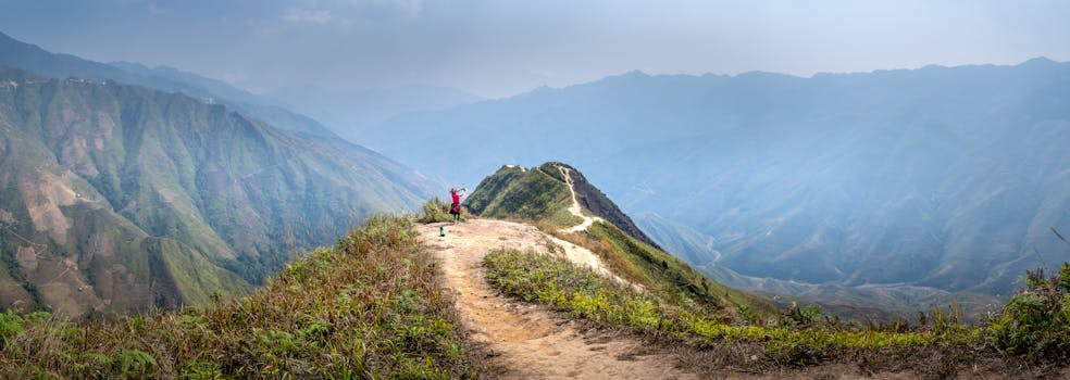 Wide angle of tourist standing on trail on hilltop surrounded by mountains in mist