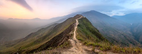 Group of travelers walking on path on grassy top of mountain ridge located in mountainous valley in mist