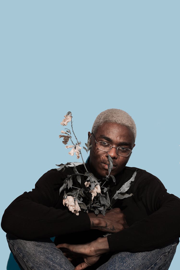 Serious Young African American Guy Resting In Studio With Dry Plants In Hands