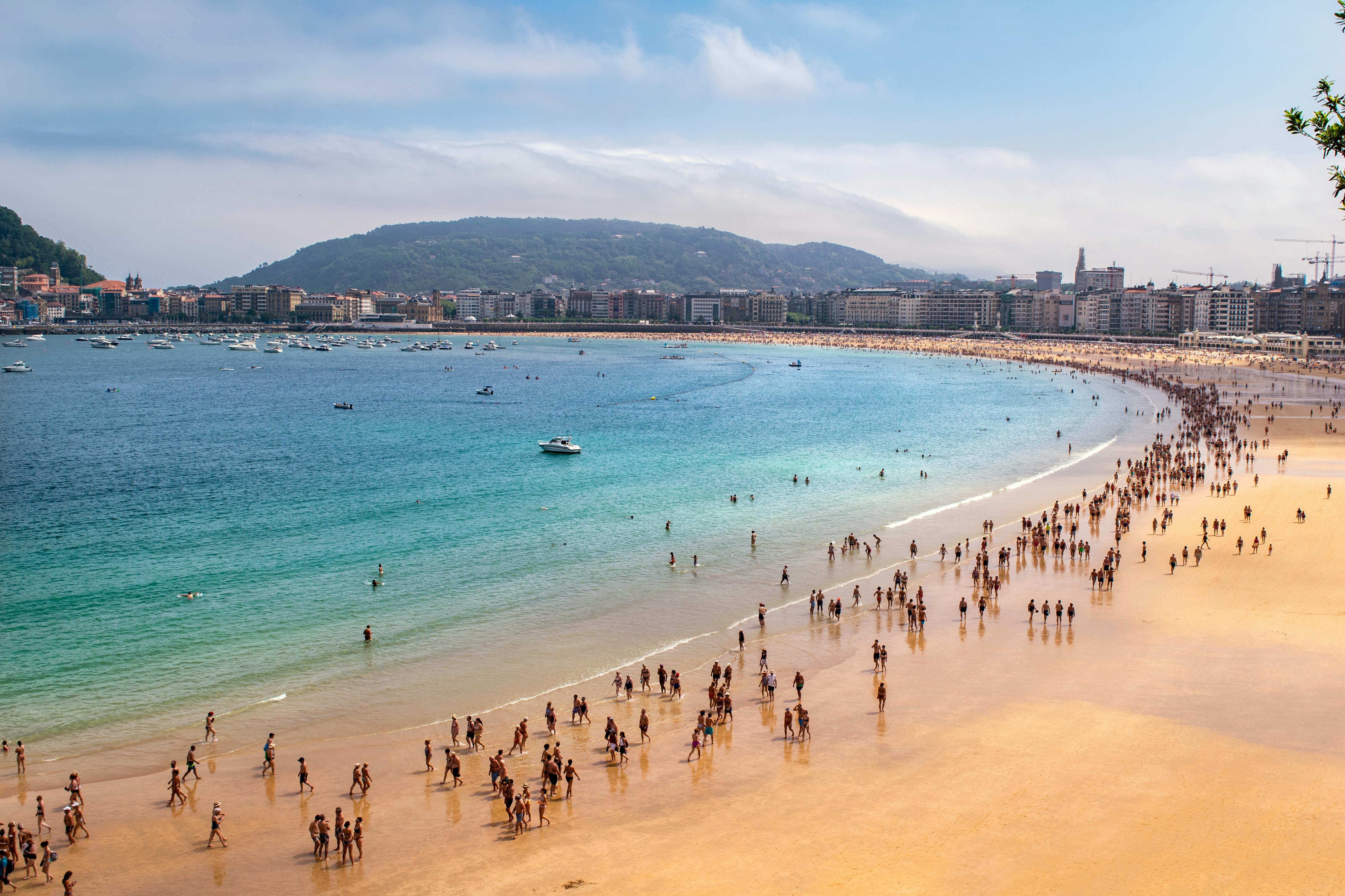 Crowds enjoy a bustling day at San Sebastián beach with clear sky and turquoise water.