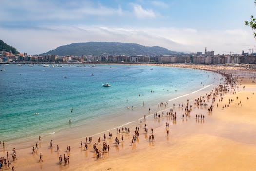 Crowds enjoy a bustling day at San Sebastián beach with clear sky and turquoise water.