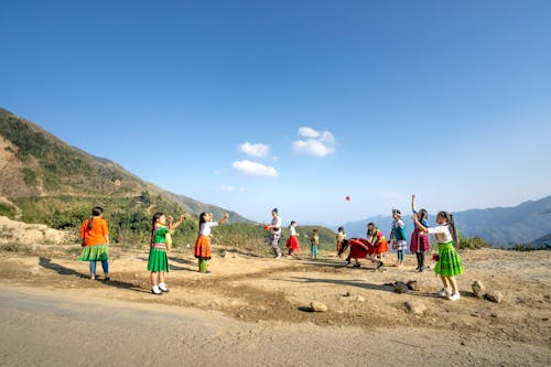 Group of local kids in colorful clothes throwing balls in air while playing near mountain ridge in countryside on summer day