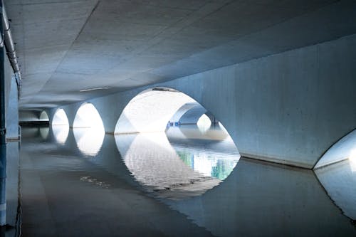 Under arched concrete bridge situated on and reflecting in rippling river in daylight