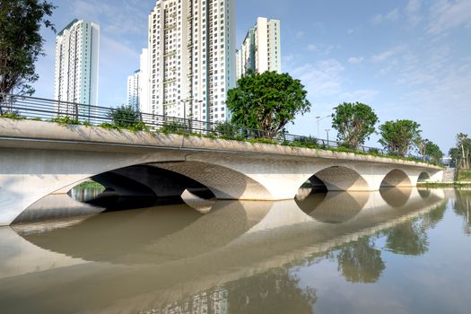White arched bridge crossing calm river near high rise residential buildings in modern city on clear sunny weather