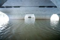 Area under concrete white bridge with arched piers situated on rippling river on sunny day