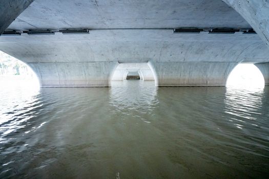 Area under concrete white bridge with arched piers situated on rippling river on sunny day