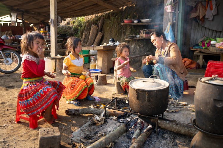 Asian Mother And Girls Sitting Near Campfire In Indigenous Village