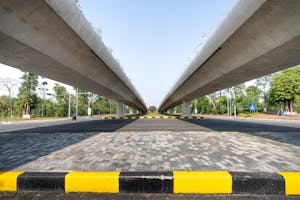 Concrete elevated highways over asphalt road between lush greenery in suburb under blue sky
