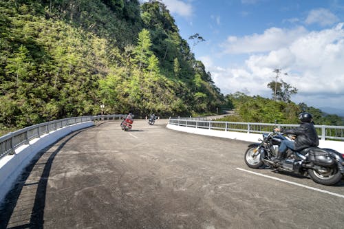 Anonymous motorcyclists driving bikes on wavy road in mountains
