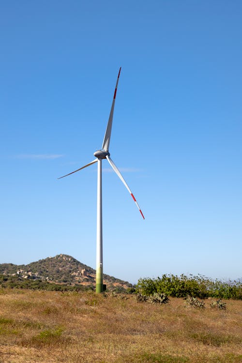 Windmill on land against mount under blue sky