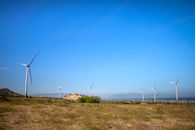 Picturesque view of air turbines on land with plants against ridges and ocean under cloudy sky in daylight