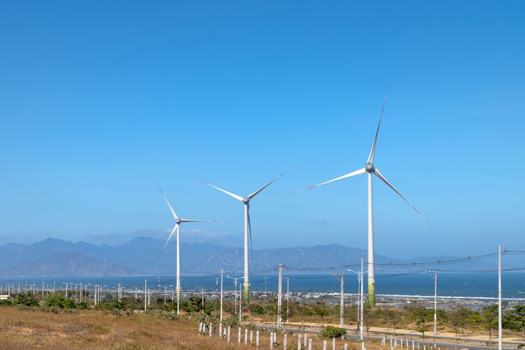 Windmills Against Sea And Ridges Under Blue Sky