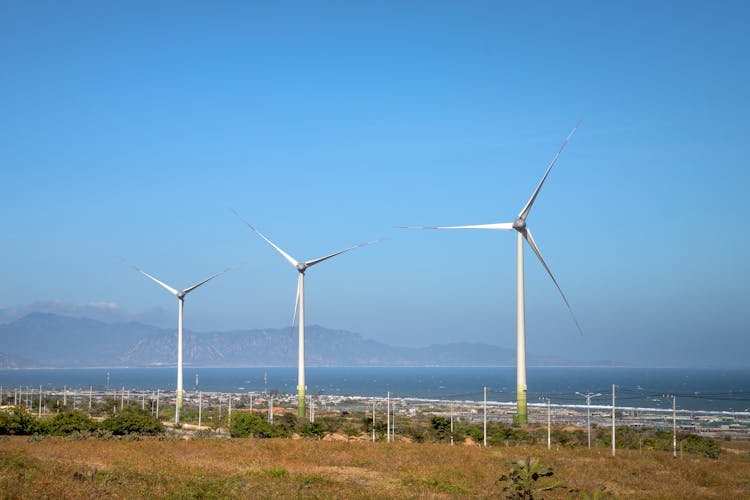 Air Turbines Against Ocean And Ridge Under Blue Sky