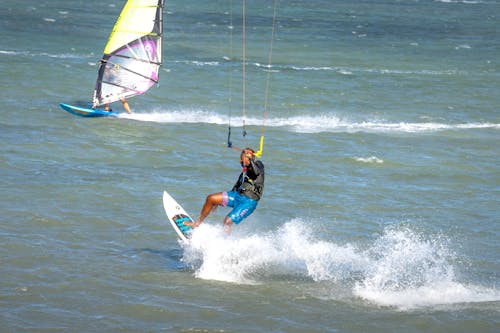 Black kite surfer with unrecognizable friend practicing kiteboarding on ocean