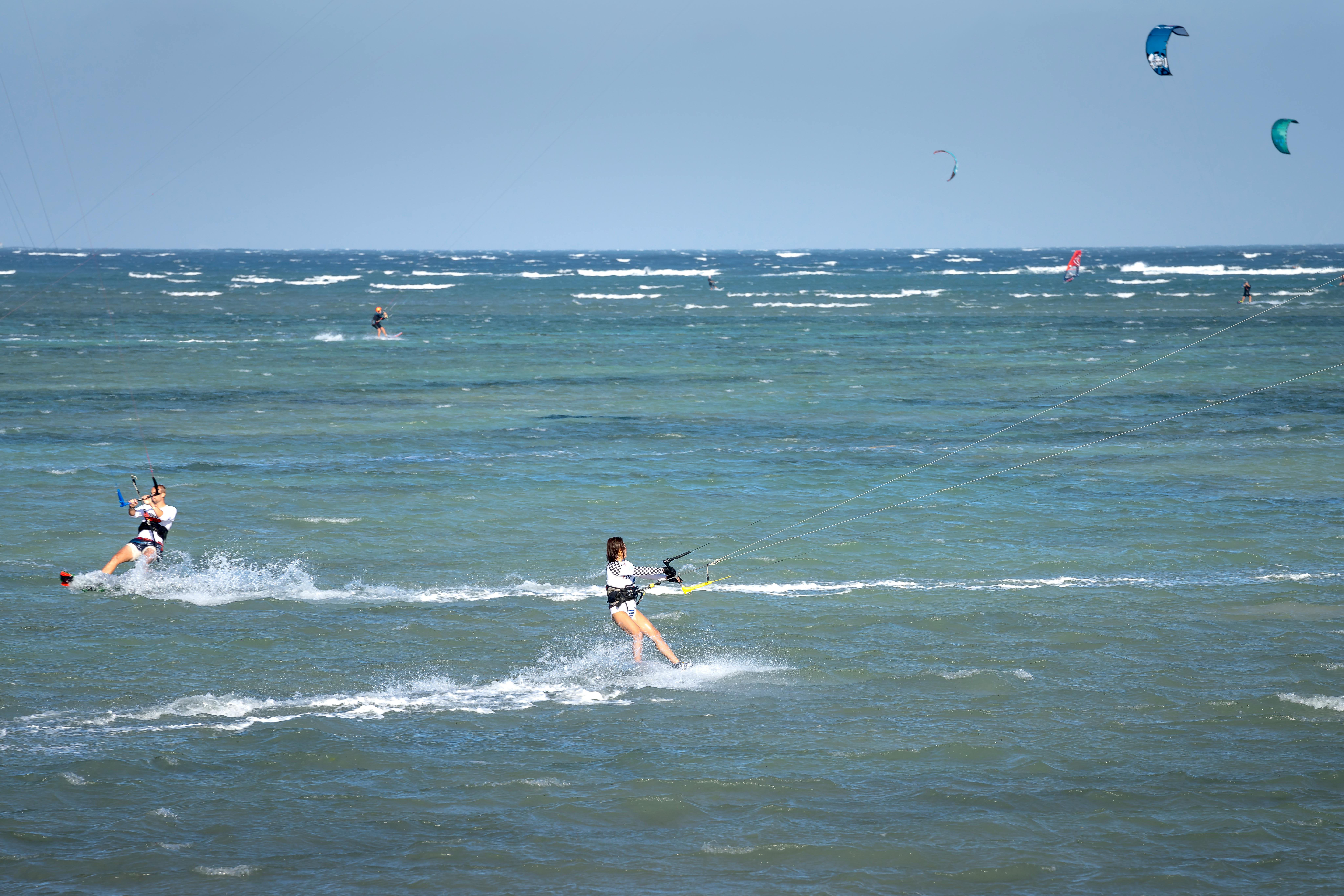 Dynamic kiteboarders riding the ocean waves, showcasing skill and excitement in a sunny, open seascape.