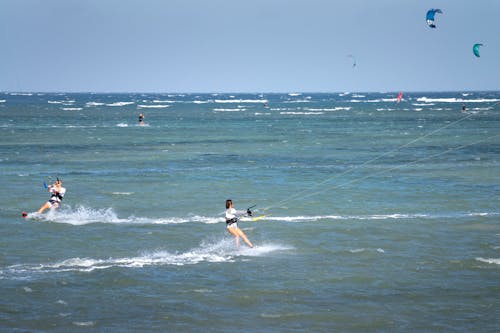 Anonymous sportswomen practicing kiteboarding on stormy ocean with horizon