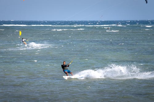 Black kite surfer with anonymous sportswoman balancing on kite boards while practicing extreme sport on wavy sea with splashes