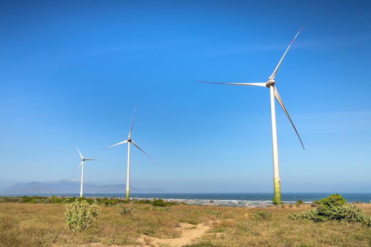 Windmills On Land Against Sea And Ridge Under Blue Sky