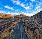 Empty straight railway tracks going through hilly area covered with grass against blue cloudy sky in rural terrain in countryside