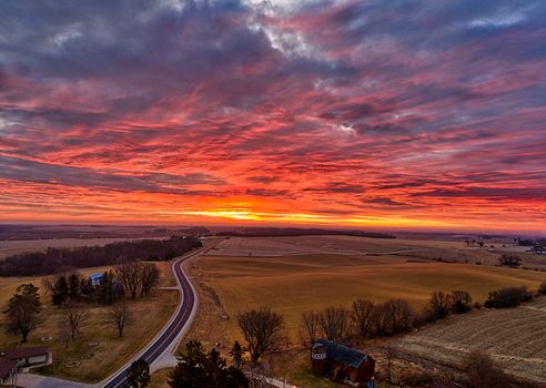 Narrow road going through grassy field with trees in suburb area with cottages against colorful sundown sky with clouds in evening time