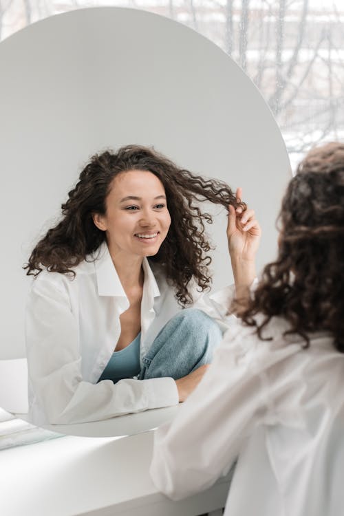 Photo Of Woman Looking In The Mirror While Holding Her Hair