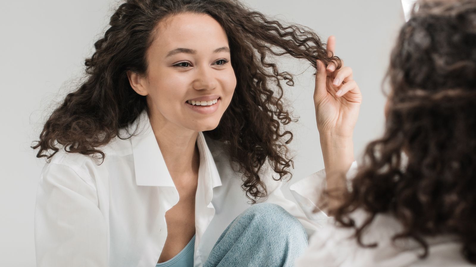 A woman smiling at her reflection in a mirror in soft natural light
