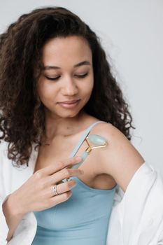 Young woman with curly hair using a jade skincare roller for self-care routine.