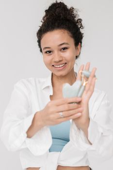 Young woman demonstrates using a jade facial roller for skincare routine.