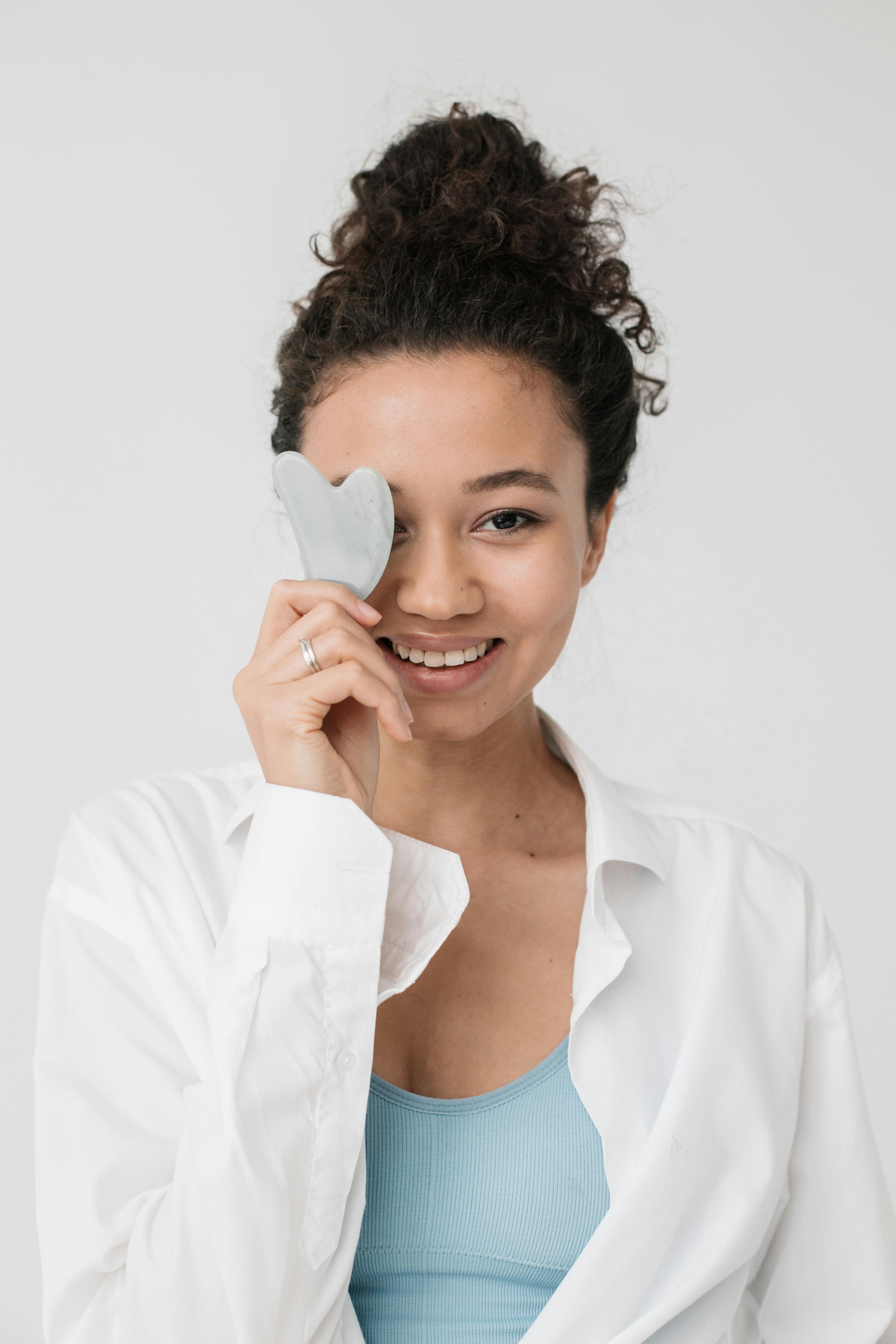 Smiling woman with curly hair using gua sha jade stone for face massage.