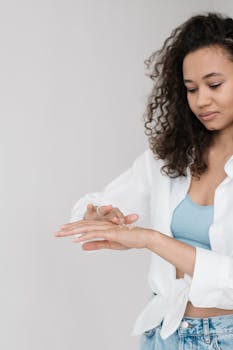 Young woman with curly hair applying skincare scrub while smiling, in a relaxed indoor setting.