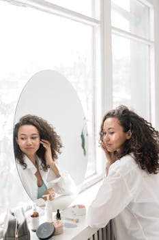 Young woman with curly hair applying skincare products in a bright room.