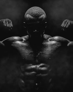 Black and white portrait of a strong muscular male athlete in a dramatic pose highlighting physique.