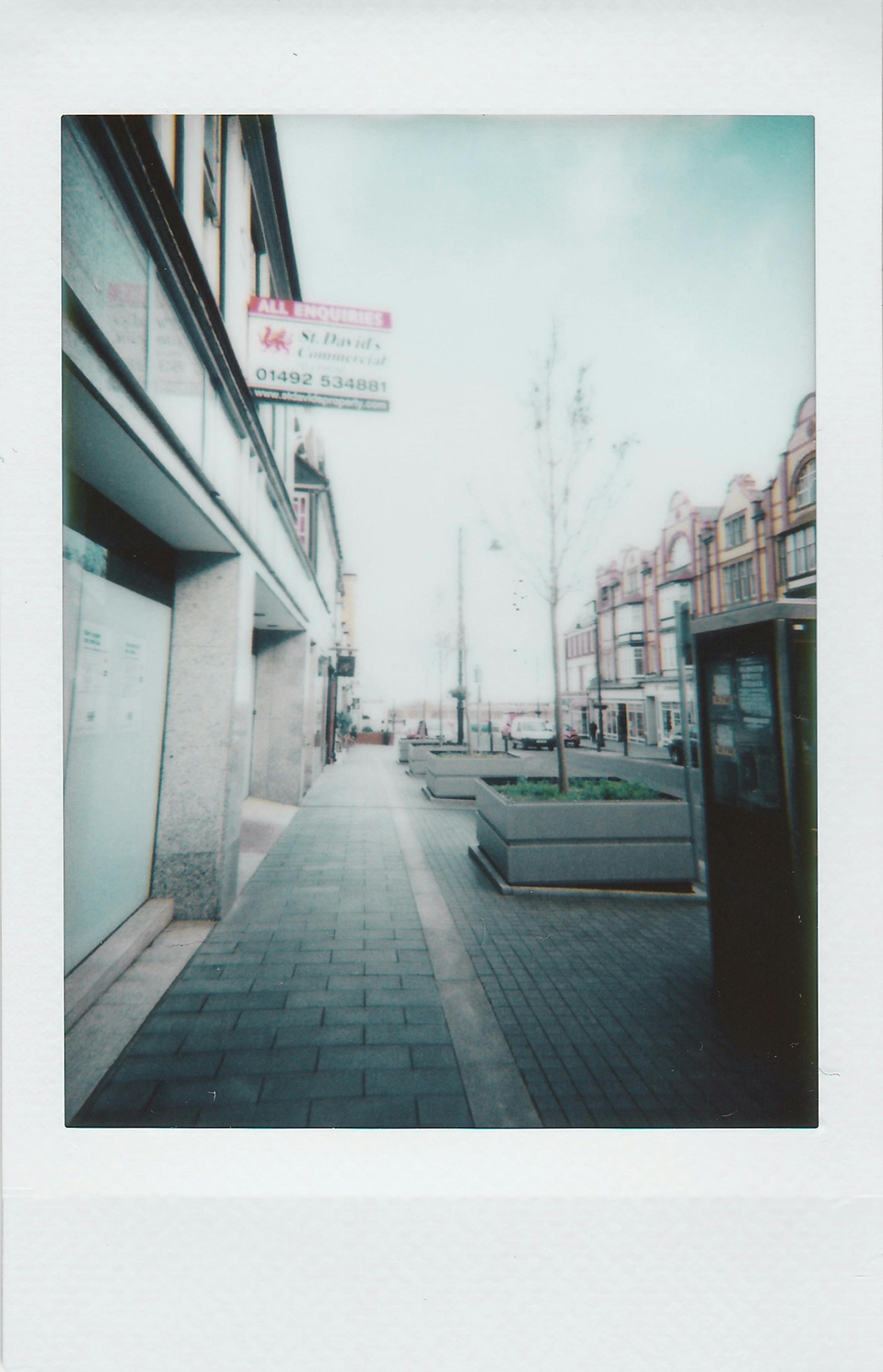 Polaroid shot of a quiet urban street with classic architecture and plant boxes.
