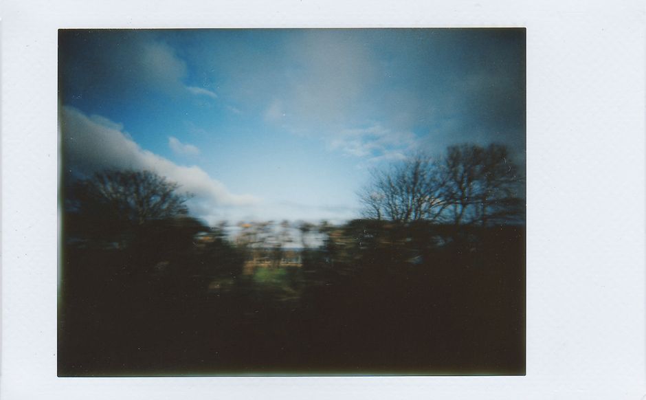 Blurred polaroid capturing trees and a blue sky with white clouds.