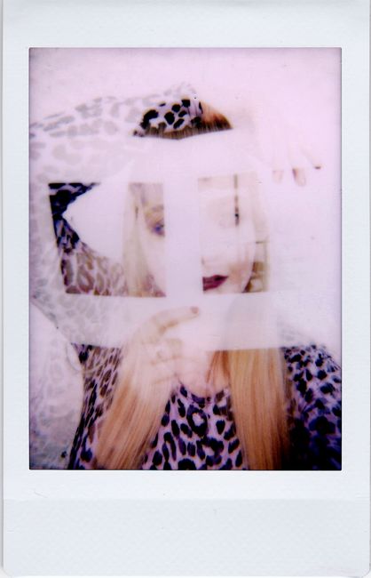 A woman in leopard print holds a square photo frame, creating an artistic polaroid effect.