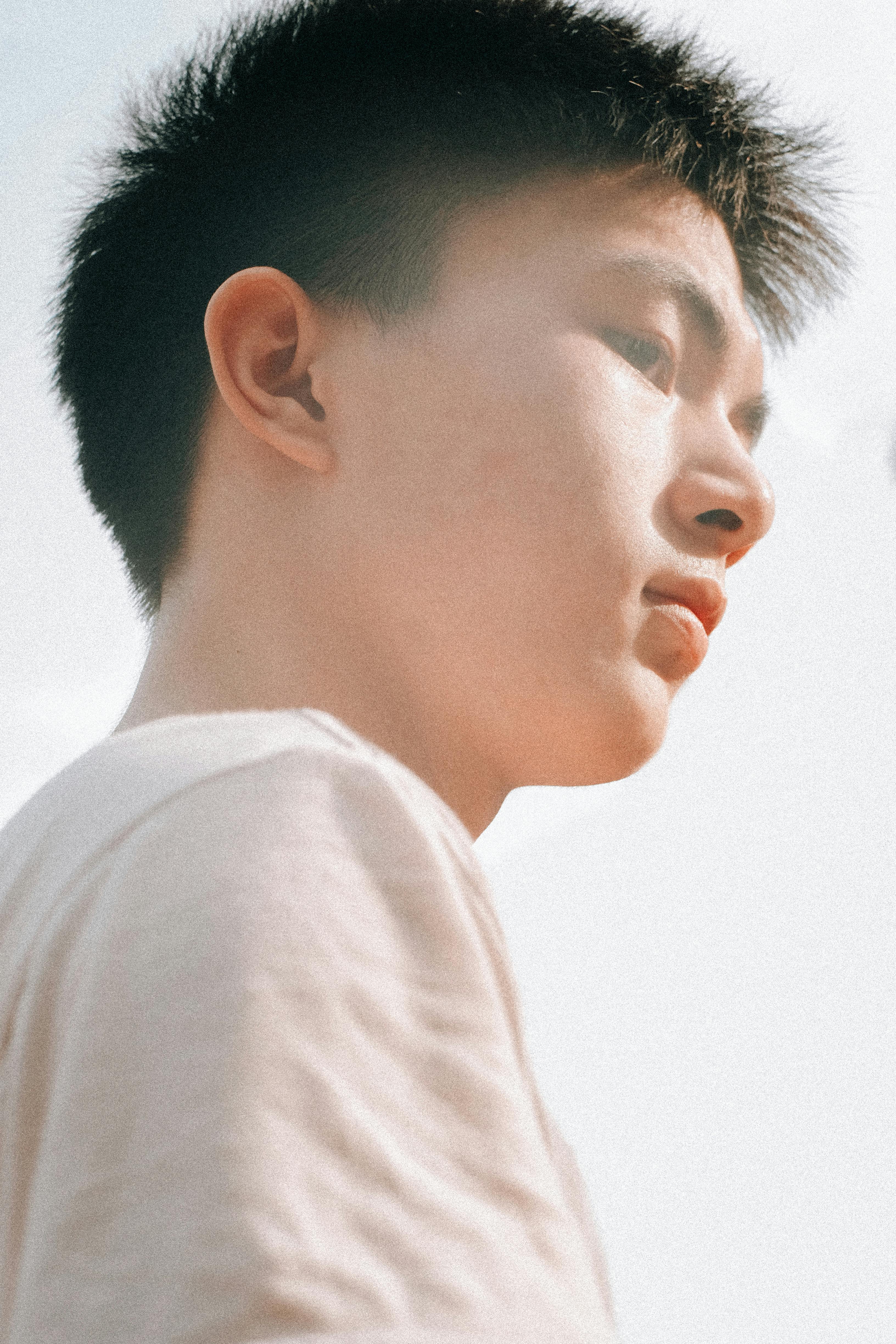 Profile of an Asian teenager in a white shirt outdoors in Vietnam, with a serene expression.