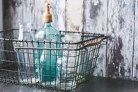 A collection of vintage glass bottles in a rustic metal wire basket on a wooden table.