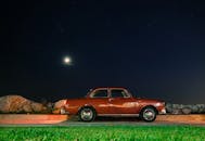 月光下，一辆红色的老爷车停在星空下，旁边是岩石和草地
