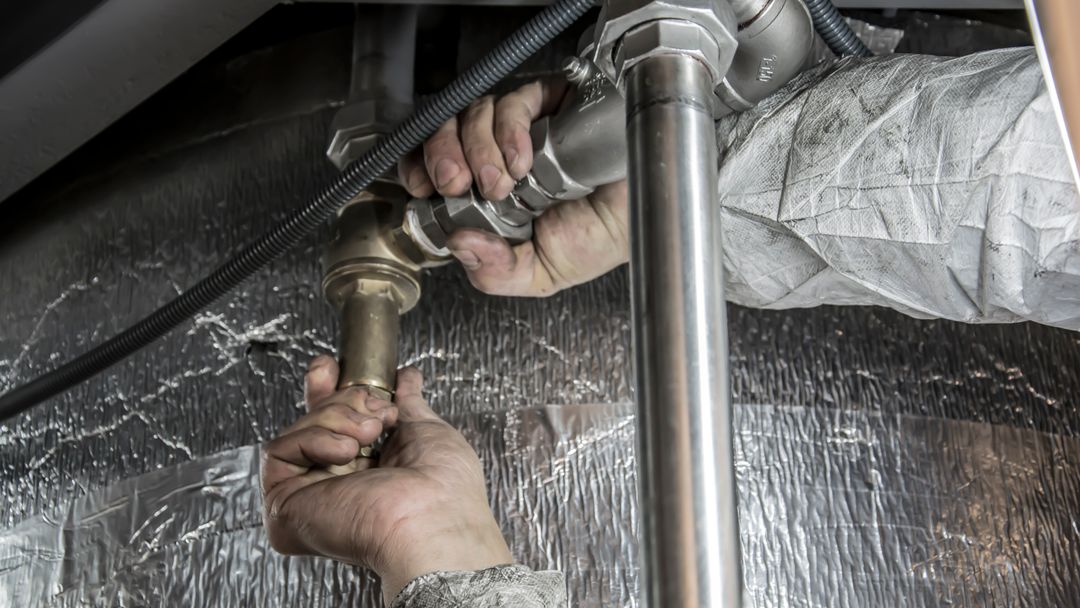 A plumber's hands fitting a steel pipe connection indoors