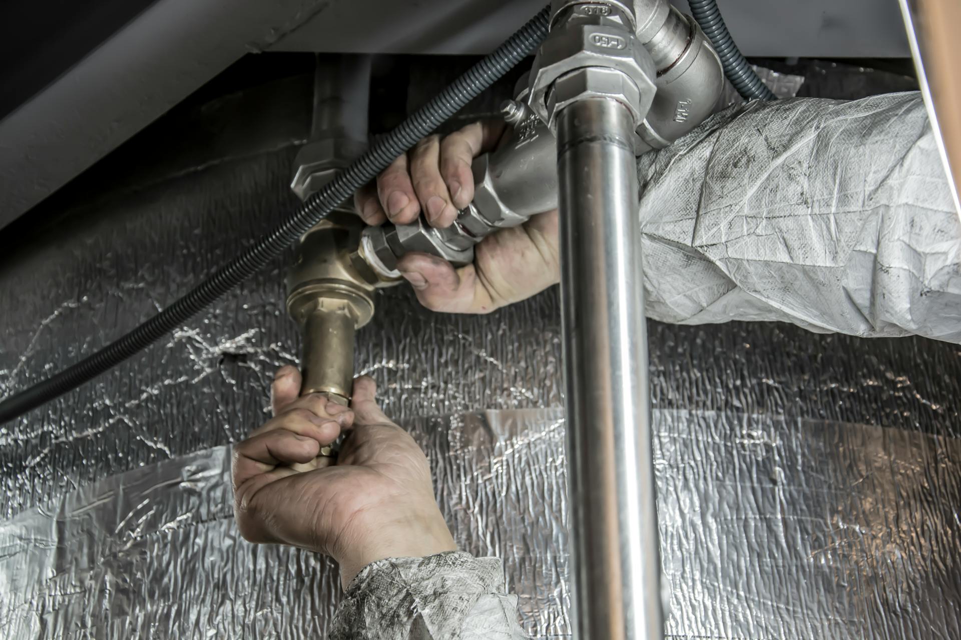 Close-up of a plumber's hands installing steel pipes indoors, showcasing skilled manual work.