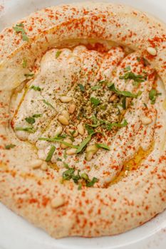 Close-up of creamy hummus topped with pine nuts, herbs, olive oil, and paprika.