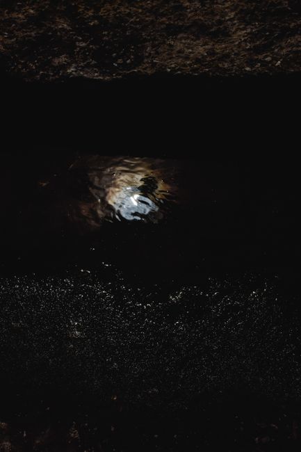 A dark and atmospheric close-up of a puddle reflecting light, captured at night.
