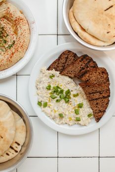 Top view of a Mediterranean spread featuring hummus, pita bread, and sliced bread on a tiled surface.